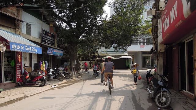 People cycling and a woman walking with flowers on a street in Hanoi, Vietnam.