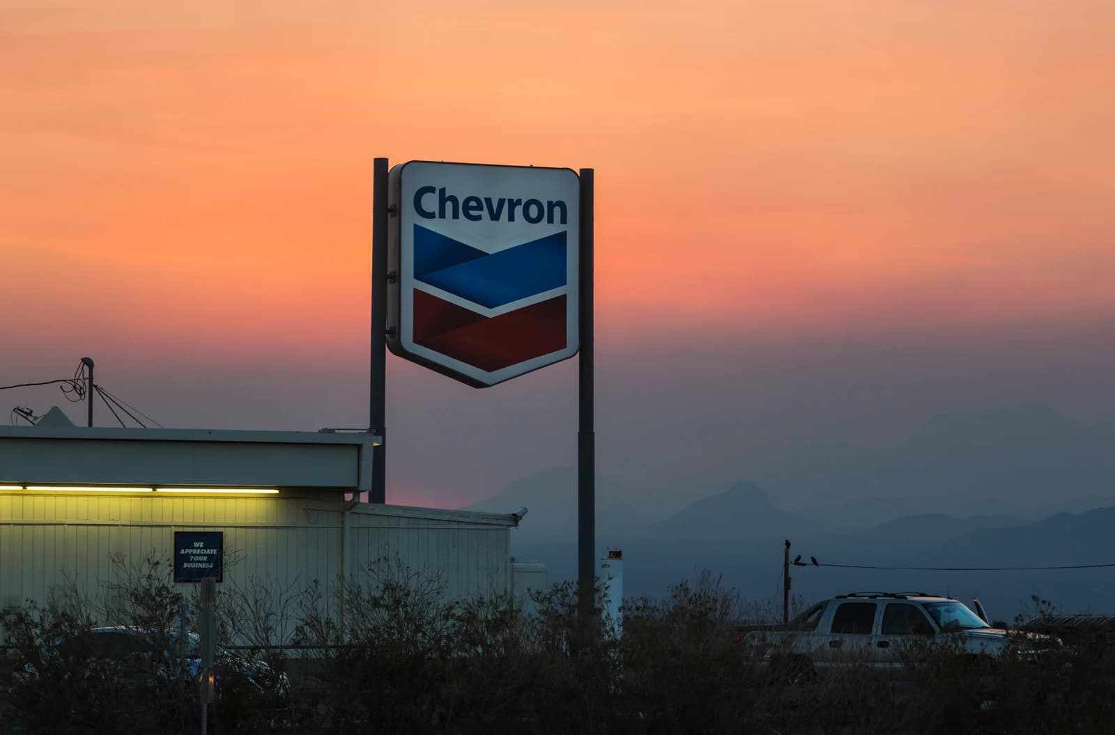 Chevron gas station sign stands against a vibrant orange and purple sunset sky.