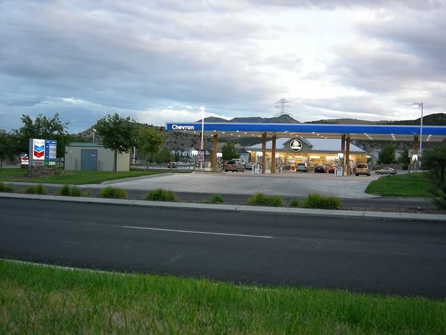 A Chevron gas station and Holiday Convenience Store at dusk with several cars.