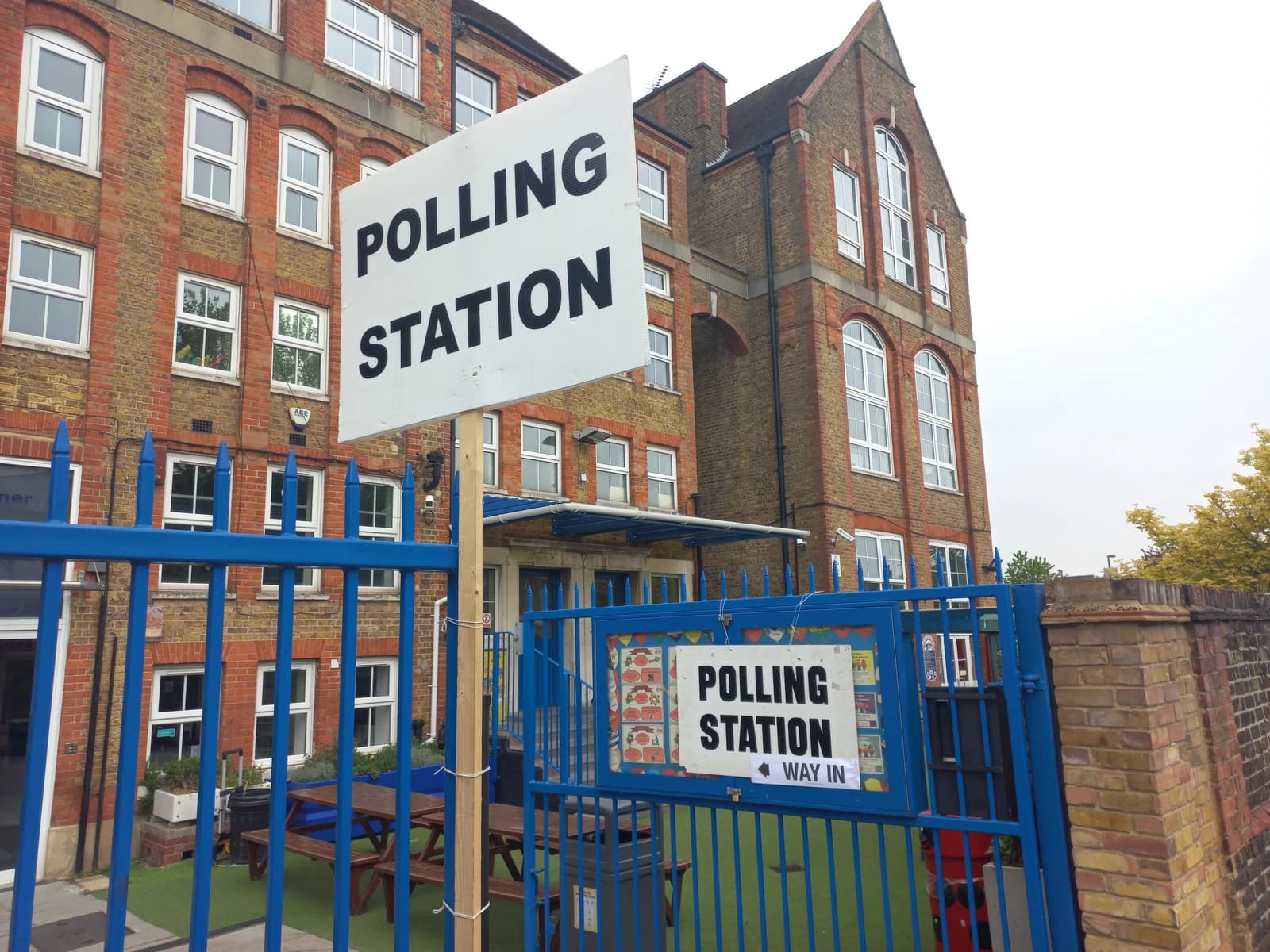 Polling station sign posted on a gate in front of a brick building.