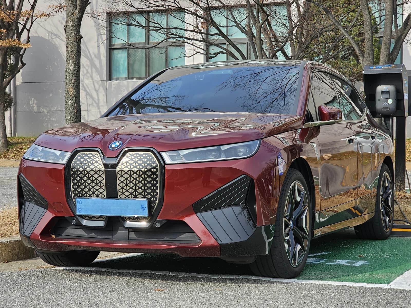 Red BMW iX xDrive40 Sport Aventurin Metallic electric car charging at a station.