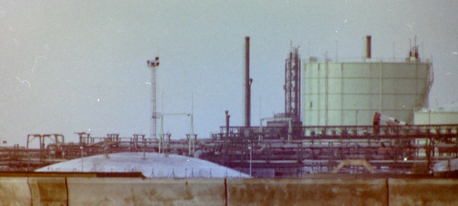 An industrial facility with large storage tanks and complex piping structures under an overcast sky.