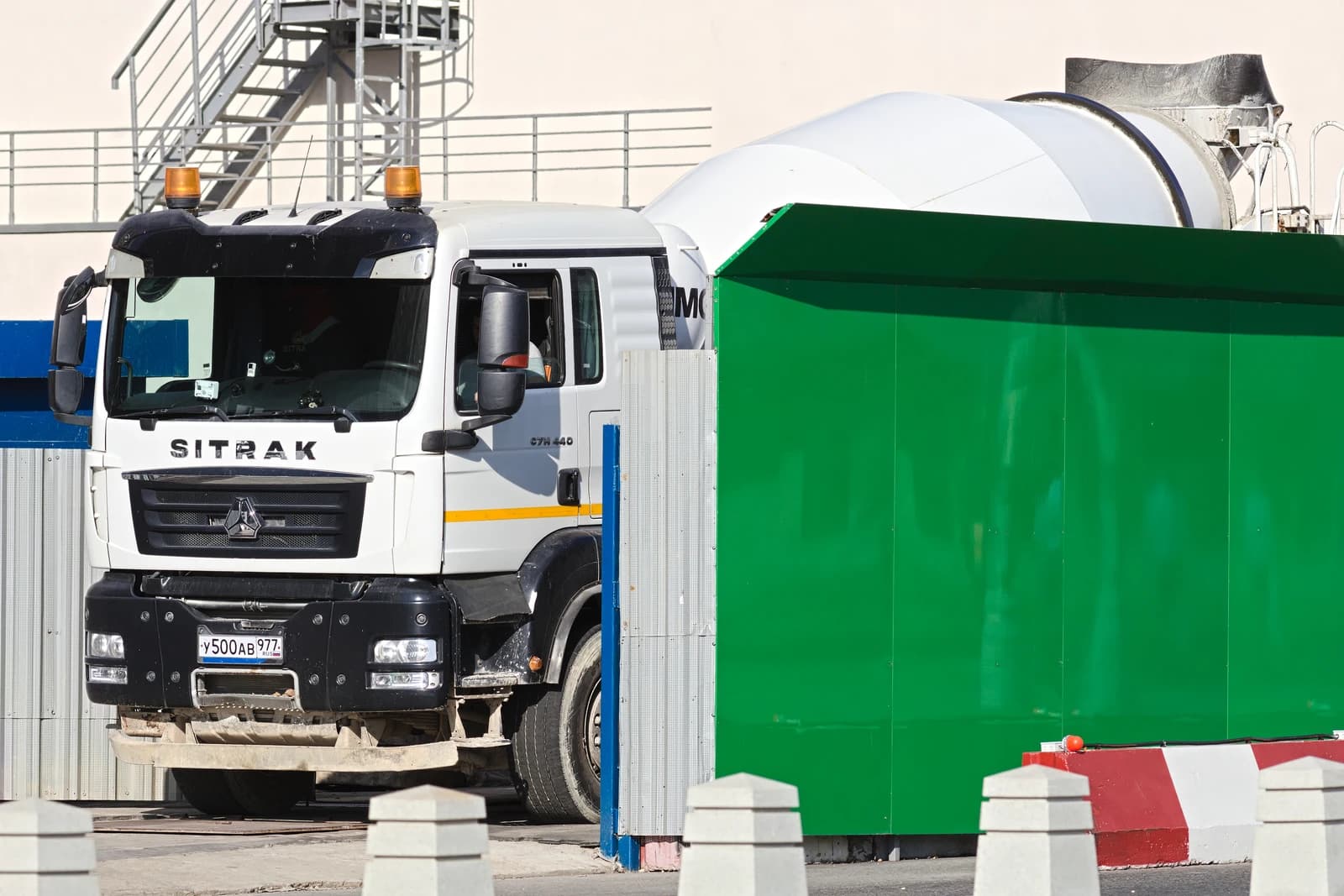 White Sitrak C7H 440 concrete mixer truck parked next to a green construction barrier.