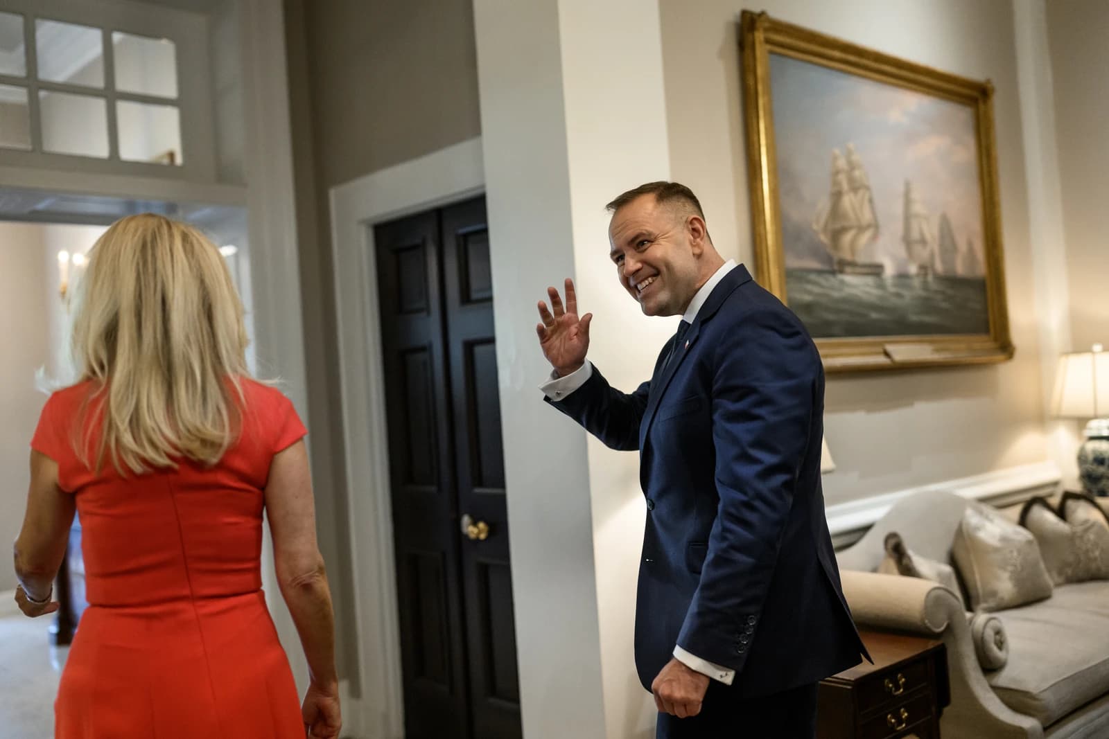 Polish President Karol Nawrocki, wearing a suit, waves to someone out of frame.