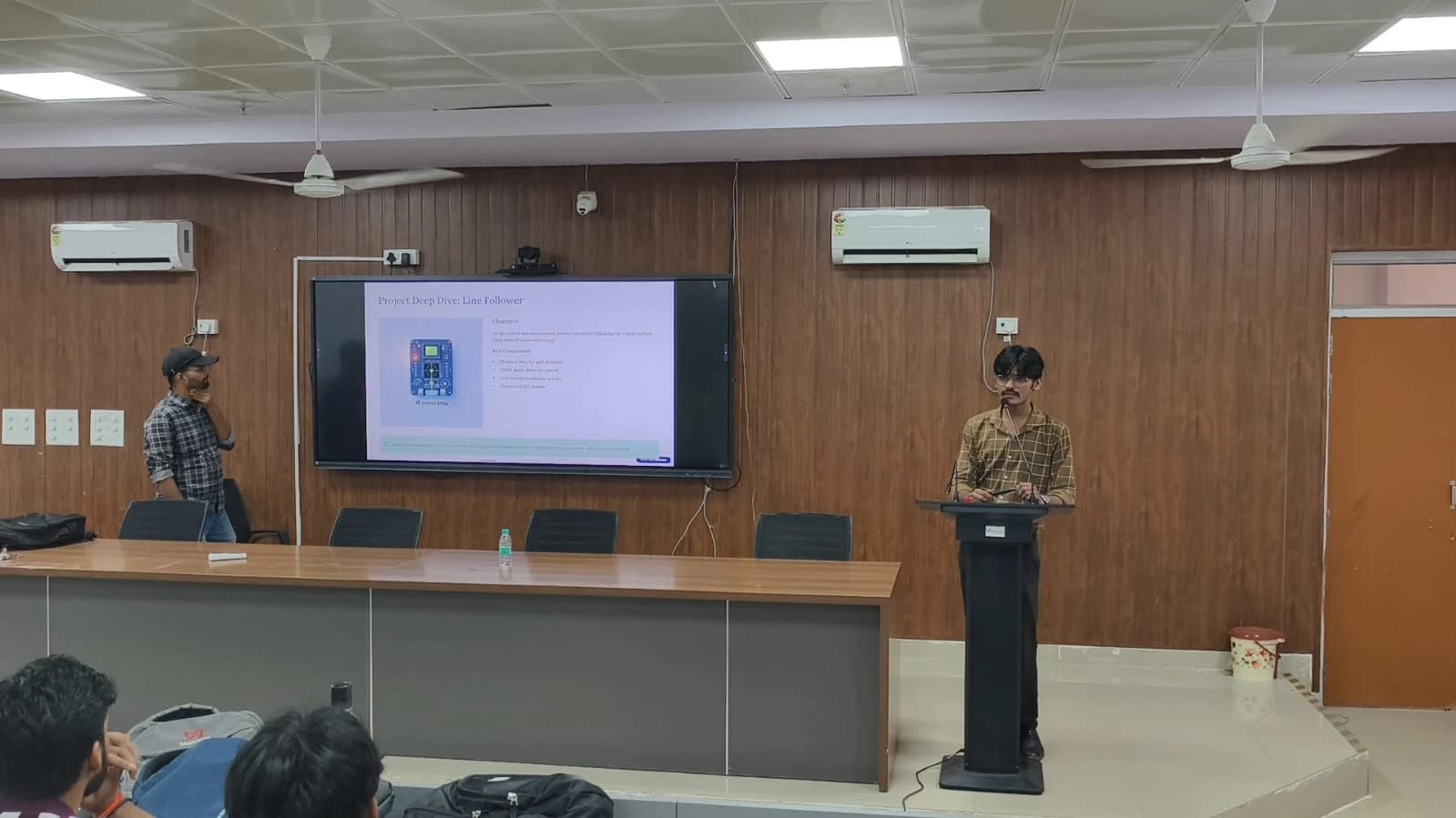 Krishna Bajpai speaking at a podium in front of a screen displaying a presentation.