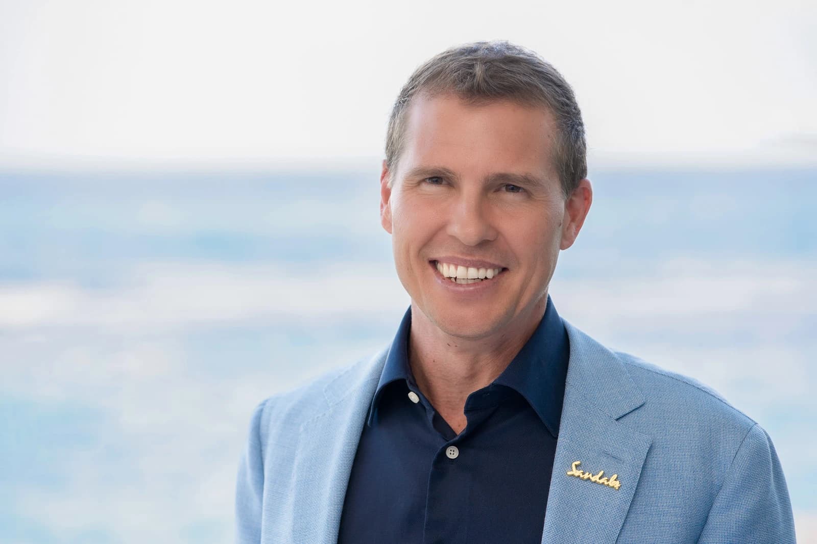 Adam Stewart, Executive Chairman of Sandals Resorts International, smiling in an outdoor setting.