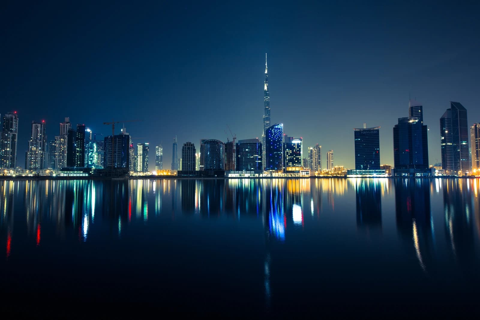 Dubai city skyline at night with illuminated buildings reflecting in the water.