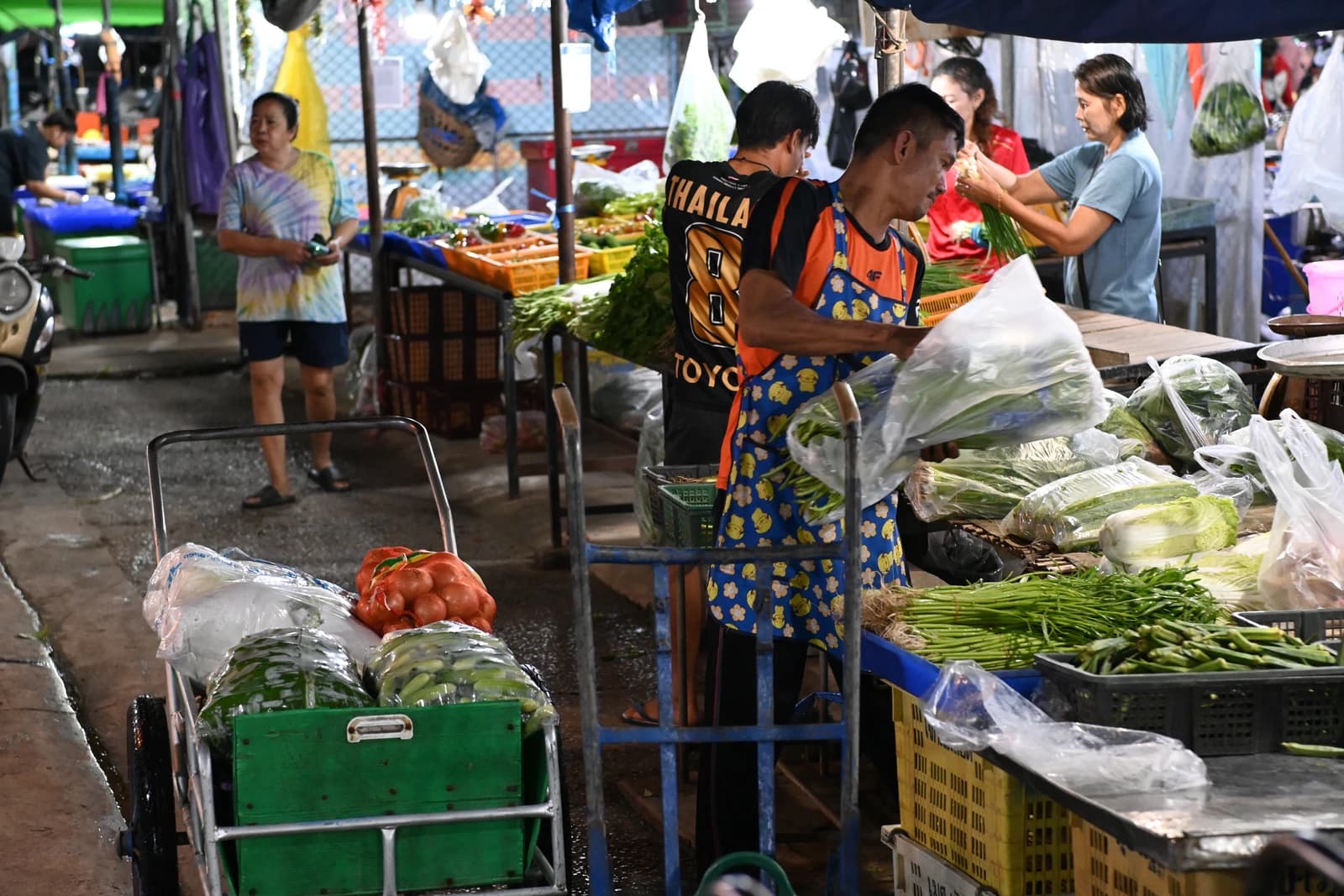 Vendors arranging fresh vegetables at a lively outdoor market stall in Asia.