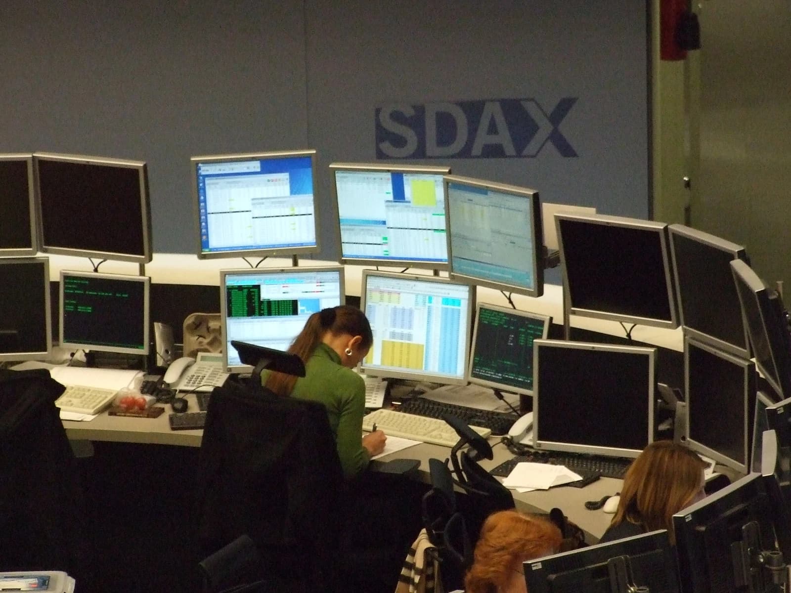 People working at computer workstations with many monitors displaying stock market data.