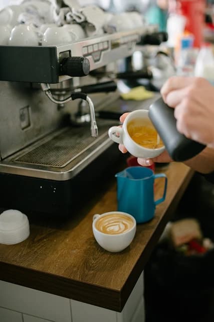 Barista pours steamed milk into a white coffee cup to create latte art.