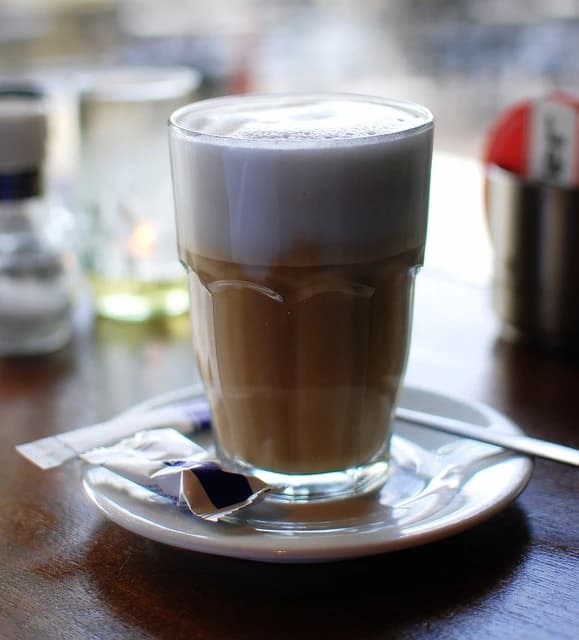 Glass of coffee with milk on a saucer with sugar packets.