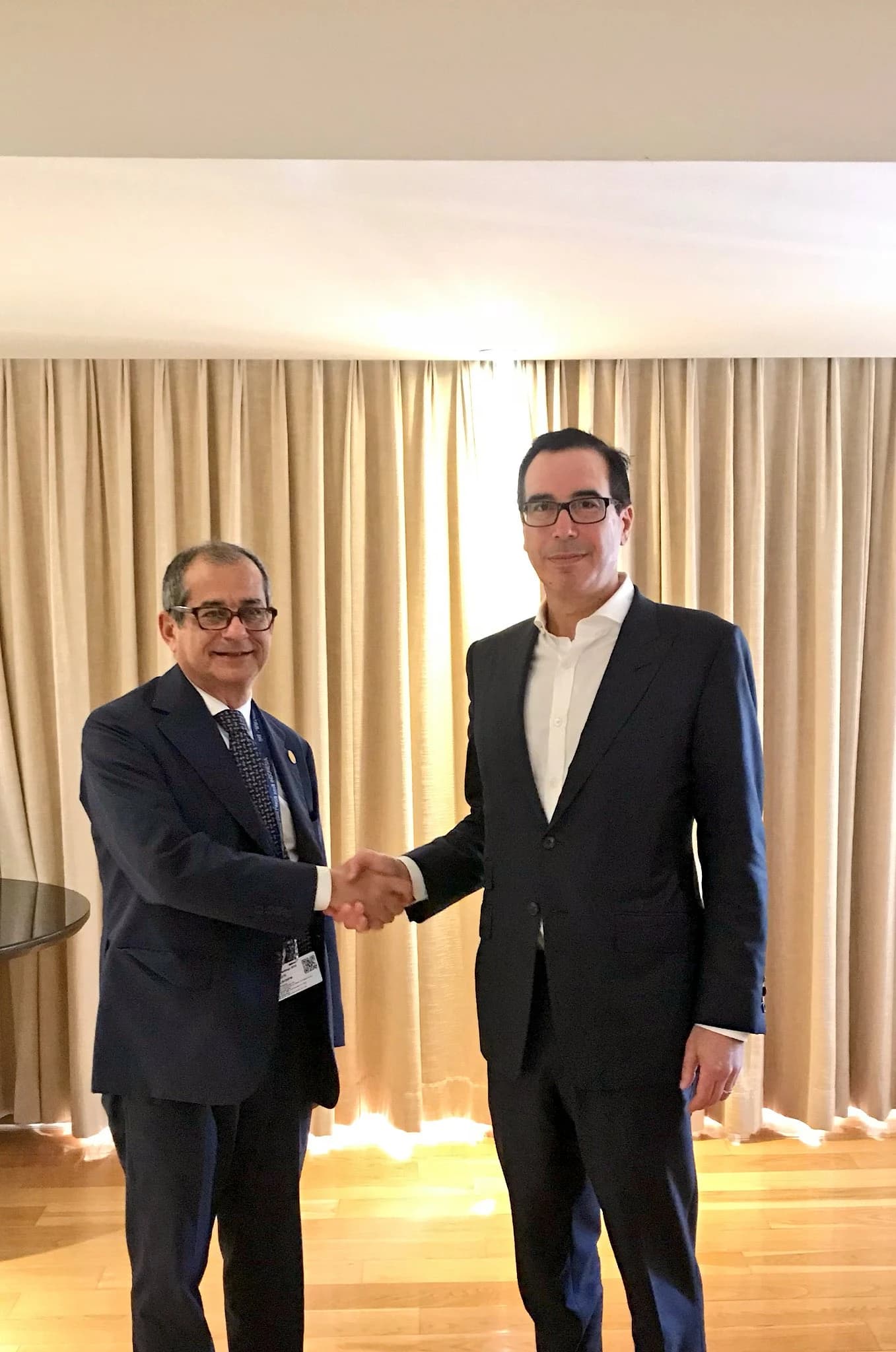 Steven Mnuchin and Giovanni Tria shaking hands at a financial meeting.
