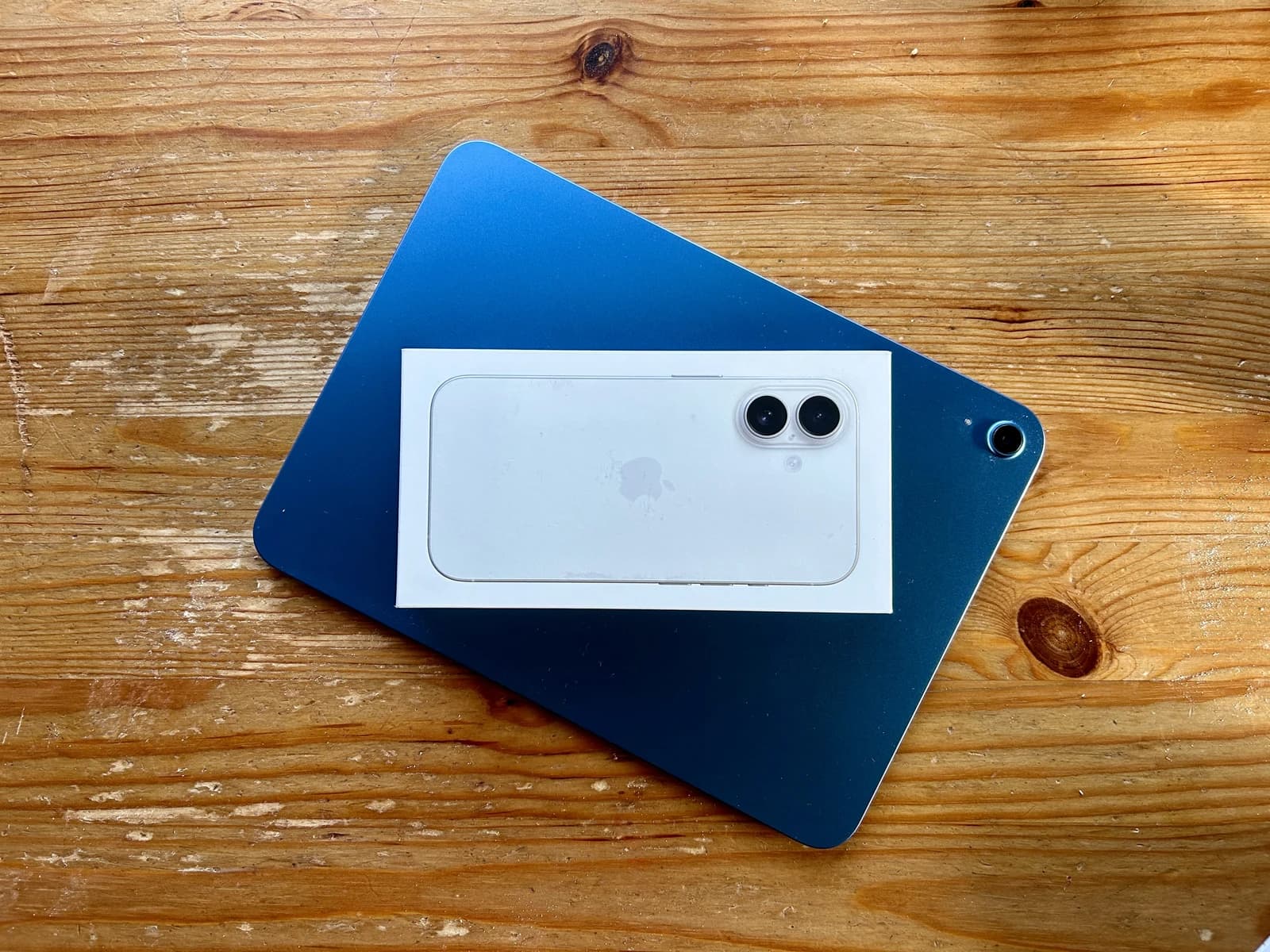 An Apple iPad 11th generation and an Apple iPhone 16 box on a wooden surface.