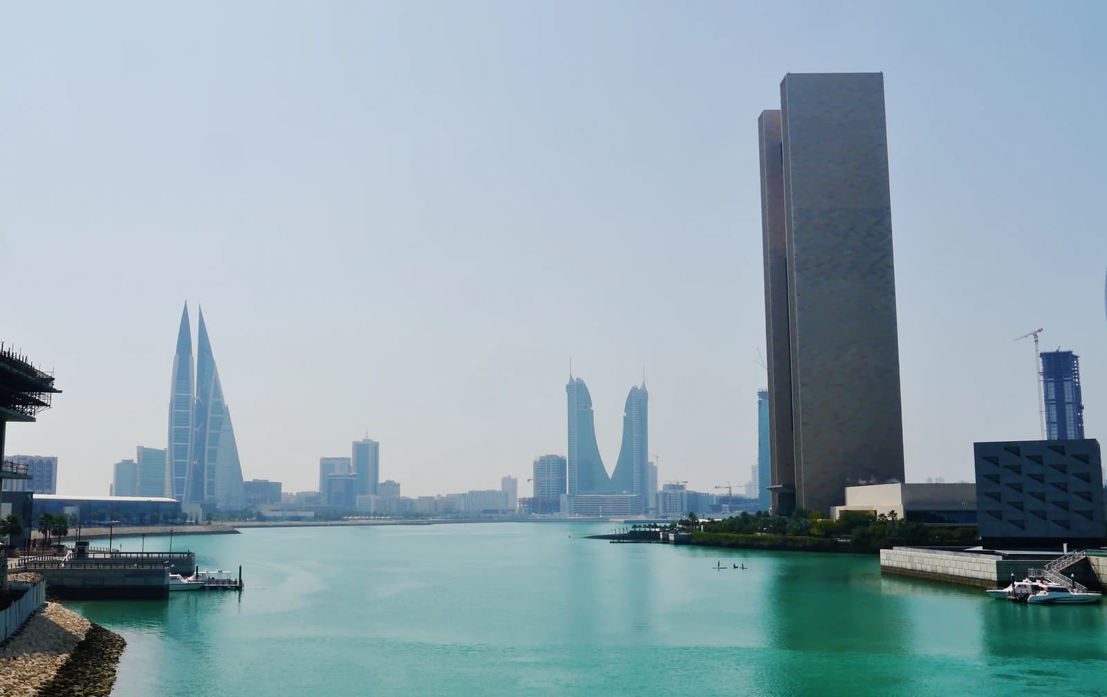 Manama skyline featuring distinctive modern buildings along a calm body of water.