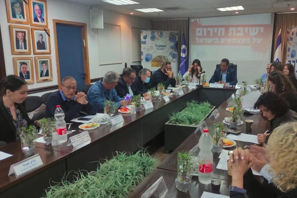 People sitting at a long table, some speaking, others listening during a meeting.