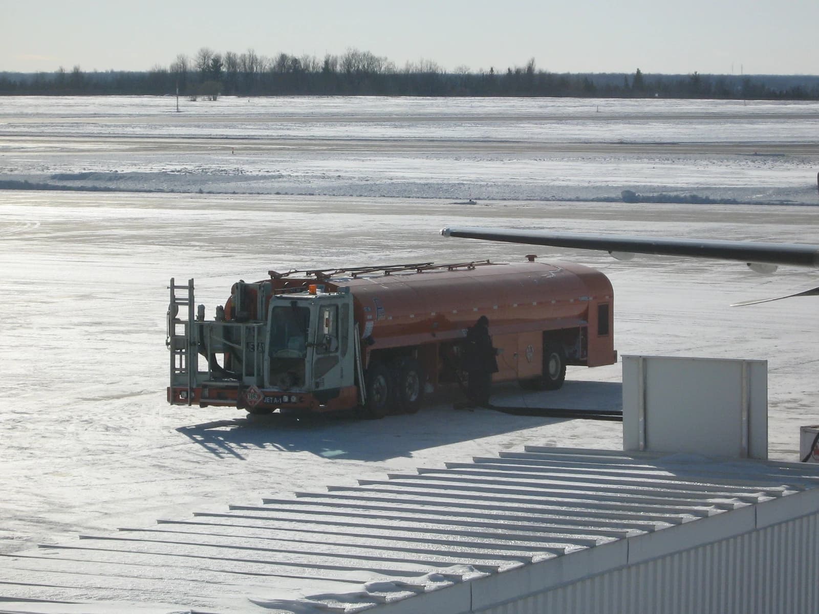 An airplane refueling truck refuels an aircraft on a snow-covered airport tarmac.