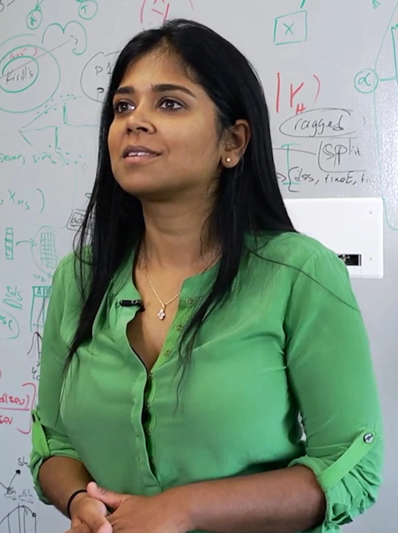 Suchi Saria, researcher for the National Science Foundation, speaking in front of a whiteboard.