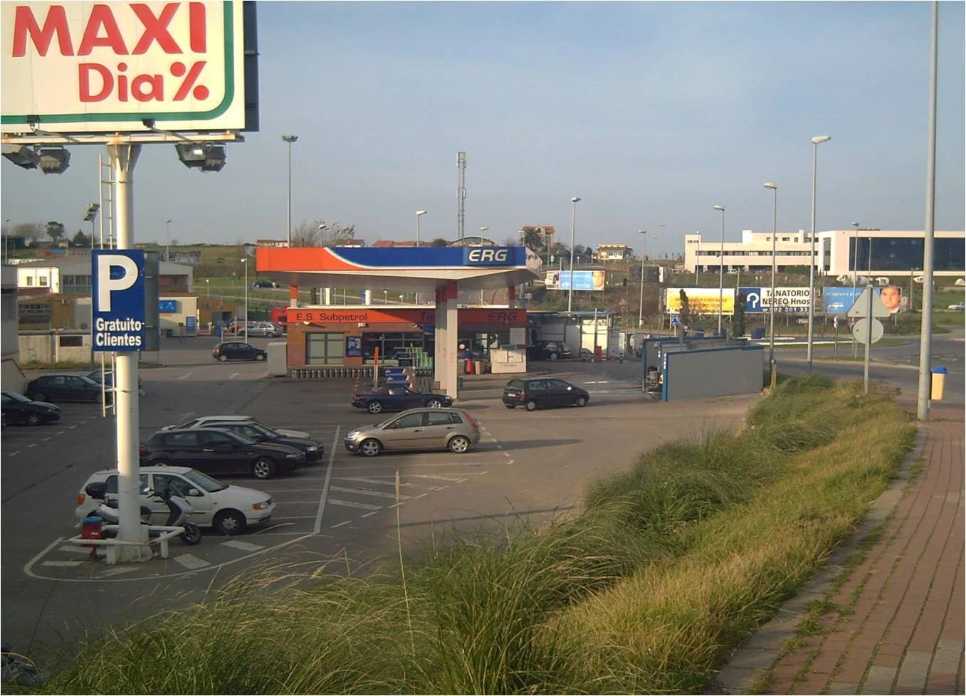 Gas station with multiple cars parked and several road signs under a clear sky.