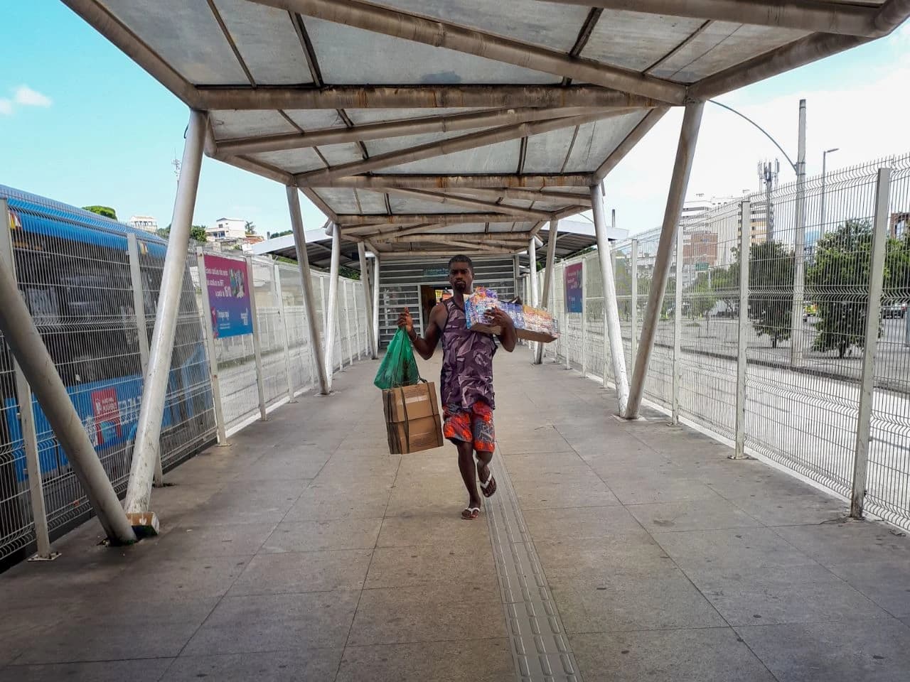 Man carrying multiple packages walks under a covered transit platform in Brazil.