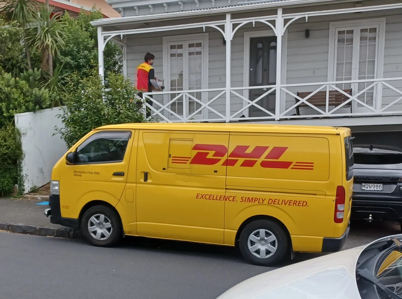 A yellow DHL delivery van parked on a street in Auckland, New Zealand.