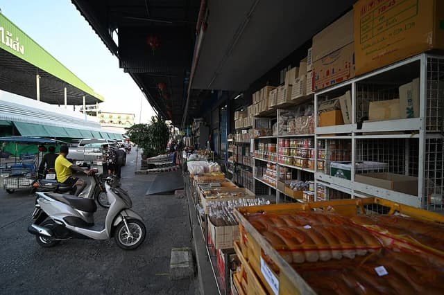 A bustling outdoor market aisle lined with shelves of packaged goods and fresh produce.