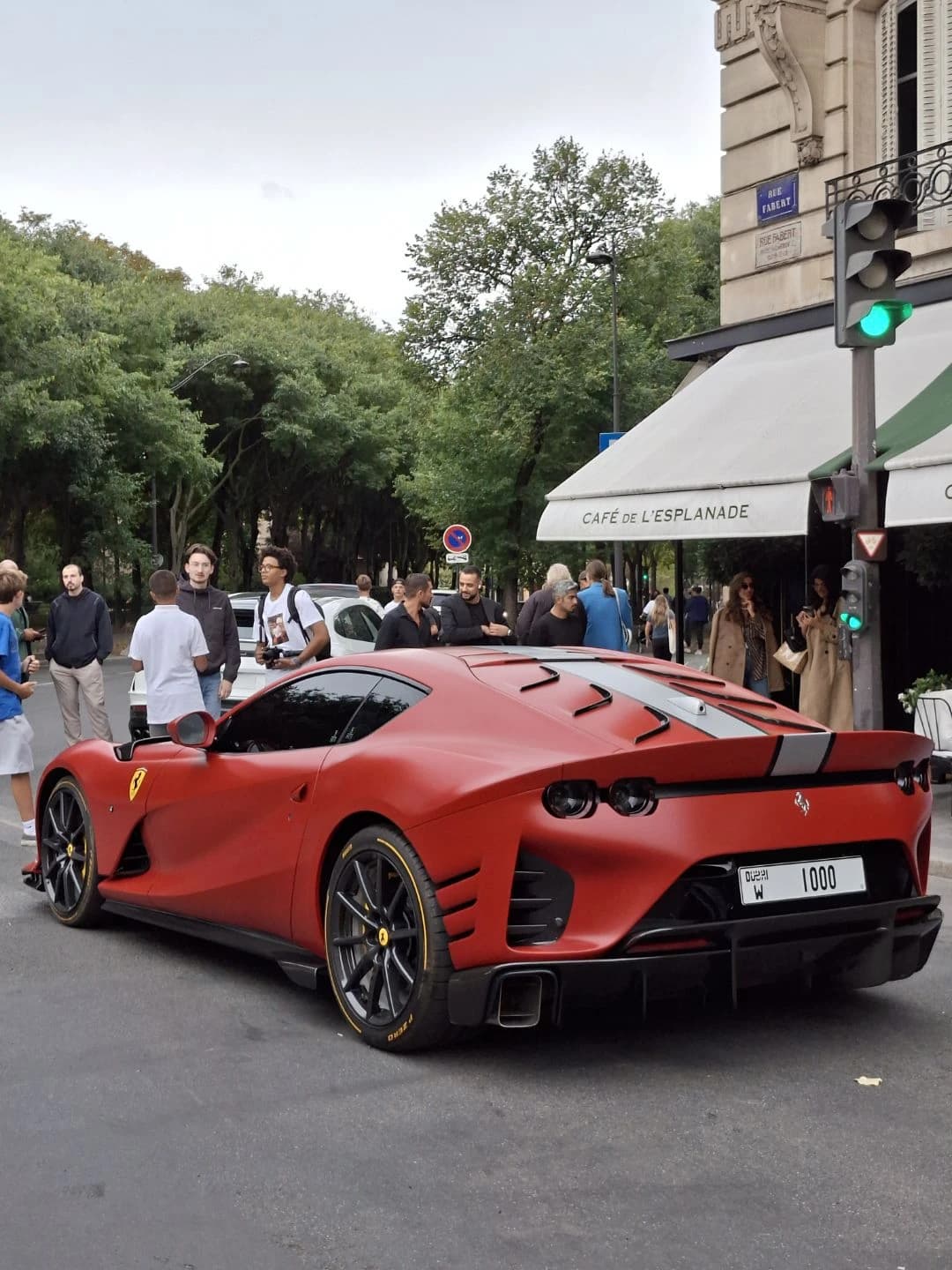 Red Ferrari 812 Competizione parked on a city street with people nearby.