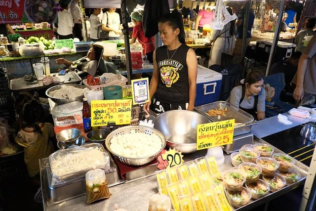 Vendor at a bustling night market food stall serving customers food.