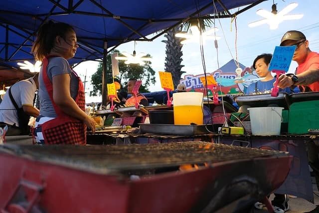 Vendor prepares dishes at a busy outdoor food stall as customers wait.