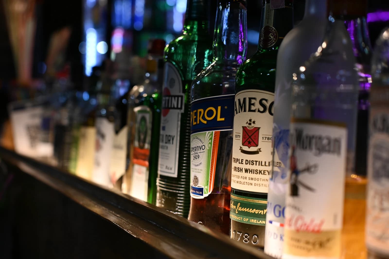 Rows of liquor bottles including Jameson, Aperol, and Martini on a dimly lit bar.