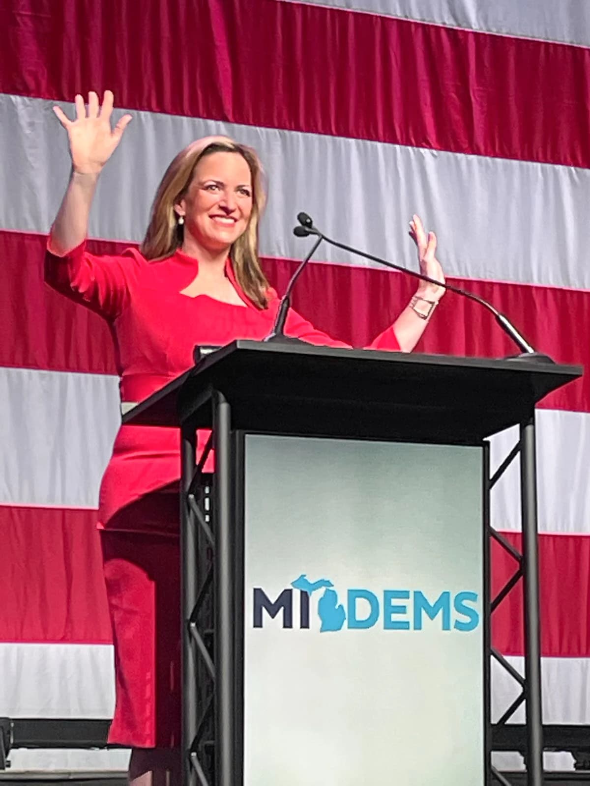 Jocelyn Benson, Michigan Secretary of State, waving from a podium at an event.