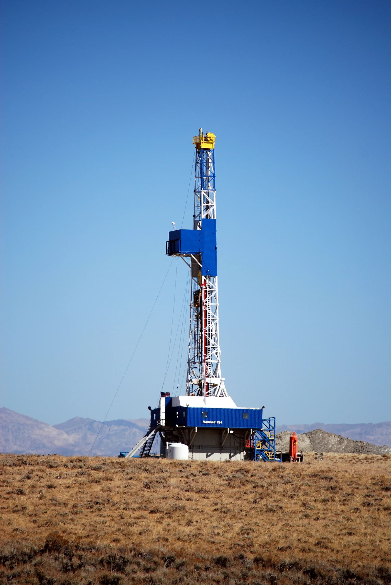 An oil and gas drilling rig with a blue and white derrick in a dry landscape.
