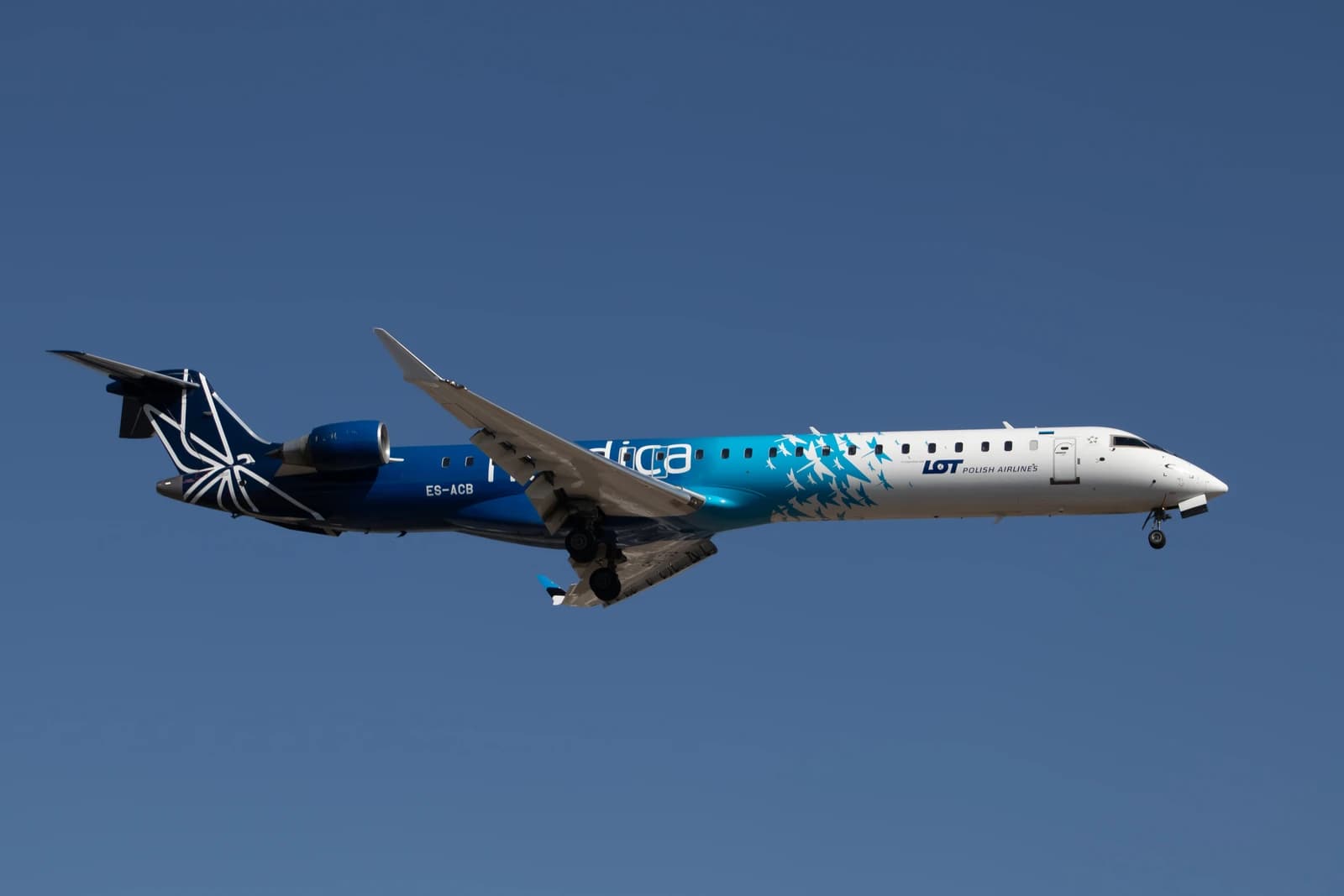 LOT Polish Airlines aircraft, registration ES-ACB, flying against a blue sky.