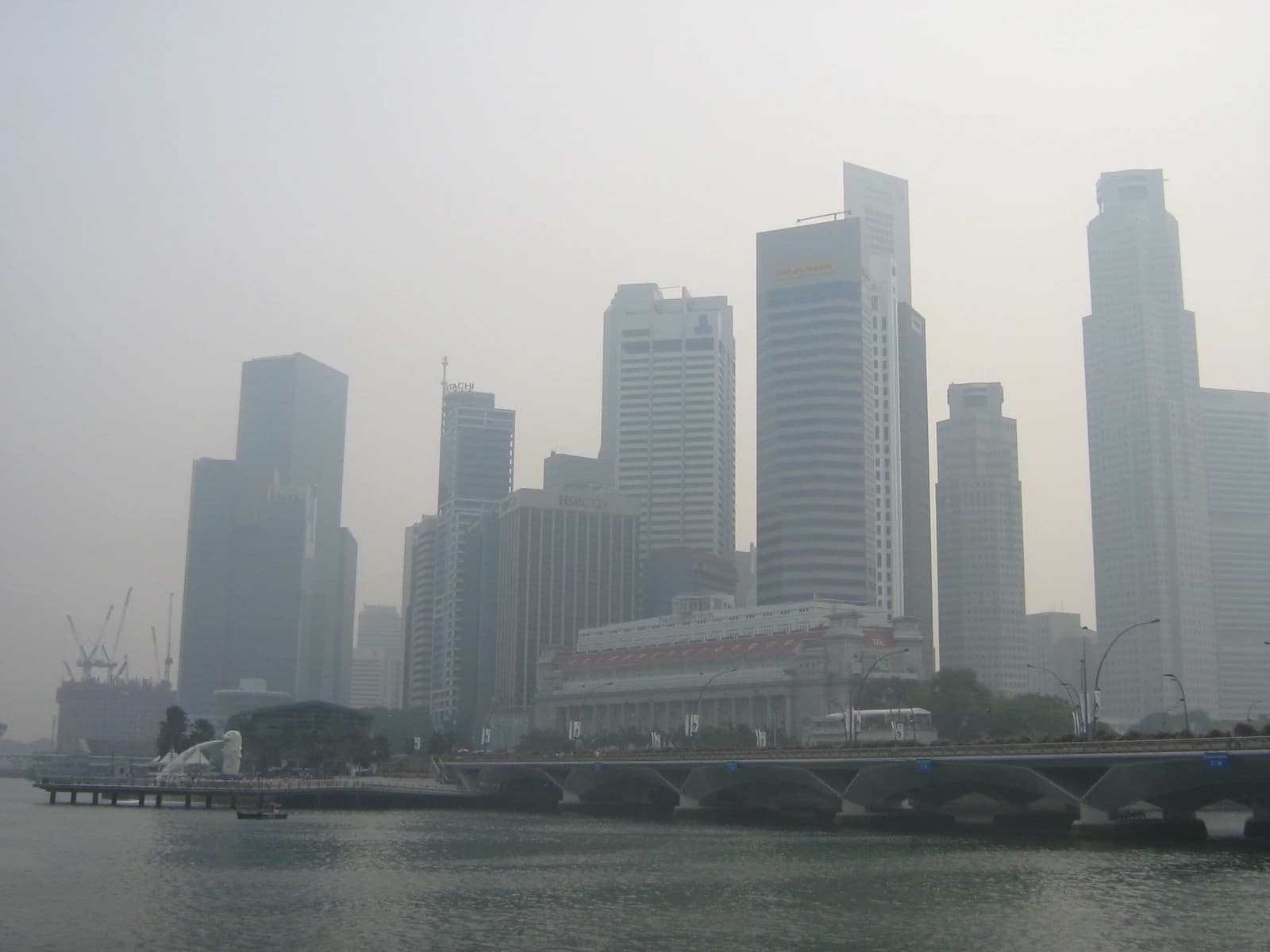 Singapore skyline with skyscrapers, Merlion statue, and a bridge obscured by haze.