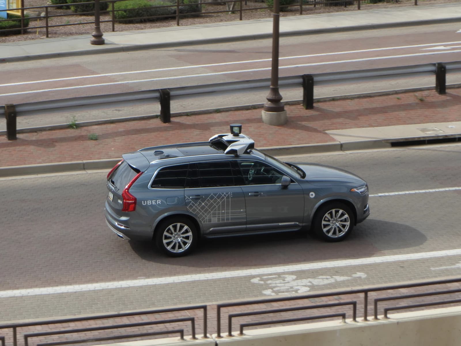 A gray Volvo XC90 SUV, equipped for self-driving, drives on a paved city street.
