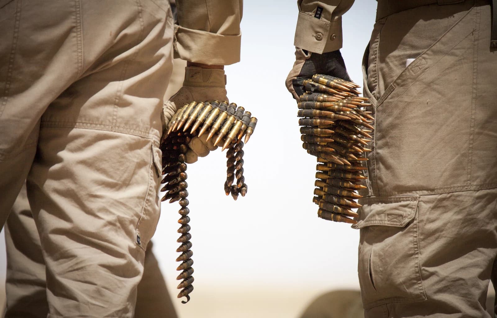 U.S. Department of Defense contractors holding belts of ammunition at a live-fire range.