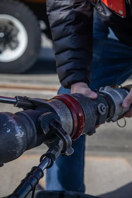 Military personnel connecting a fueling hose to an aircraft.