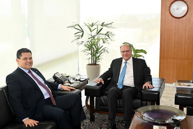 Senator Davi Alcolumbre sitting and smiling next to another man in an office.