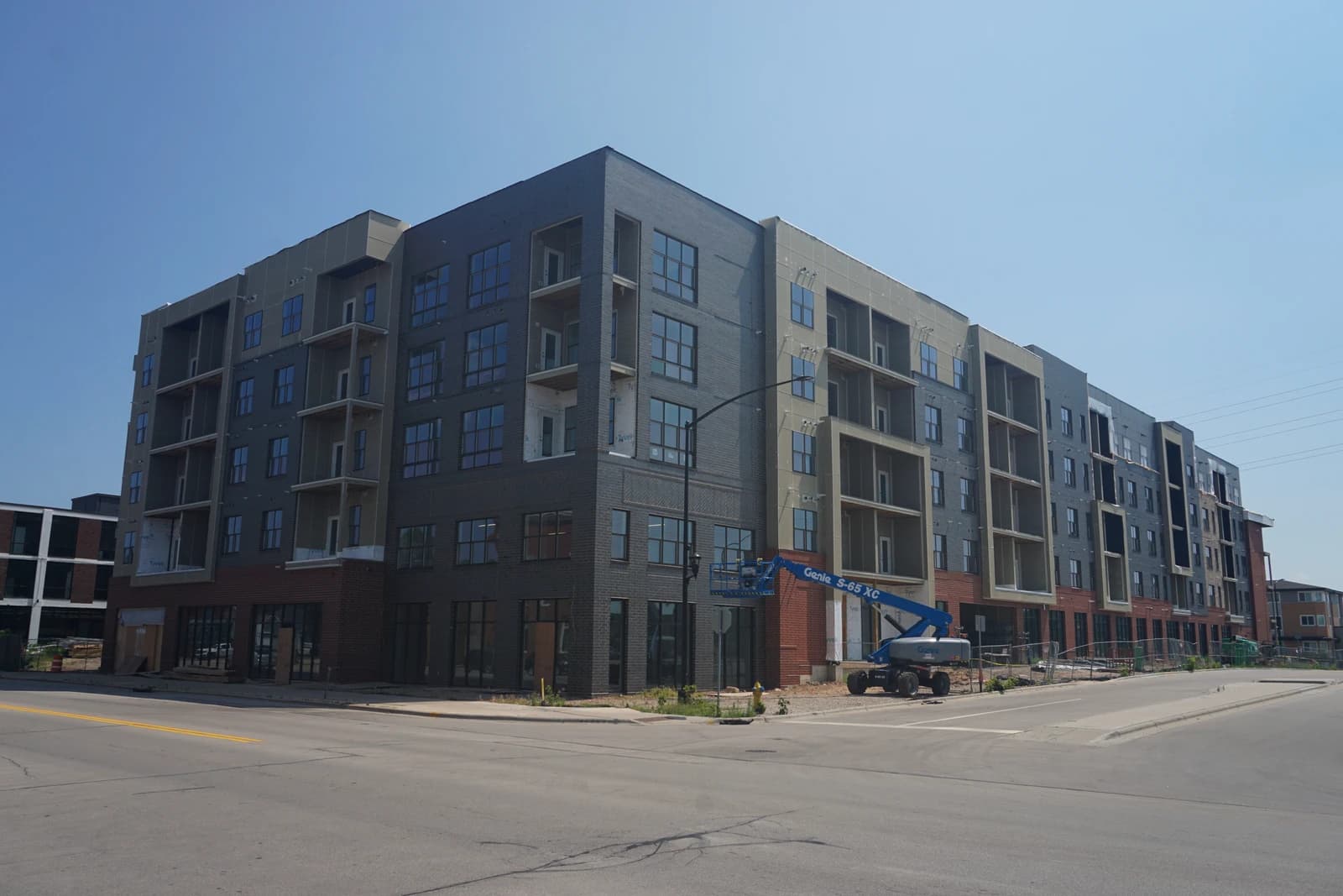 Apartment building under construction with gray and brick exterior, a Genie lift nearby.