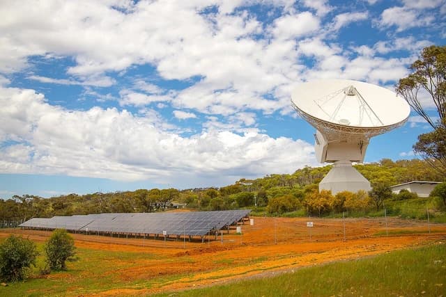 Solar panel array and large satellite dish on a hill in a rural setting.