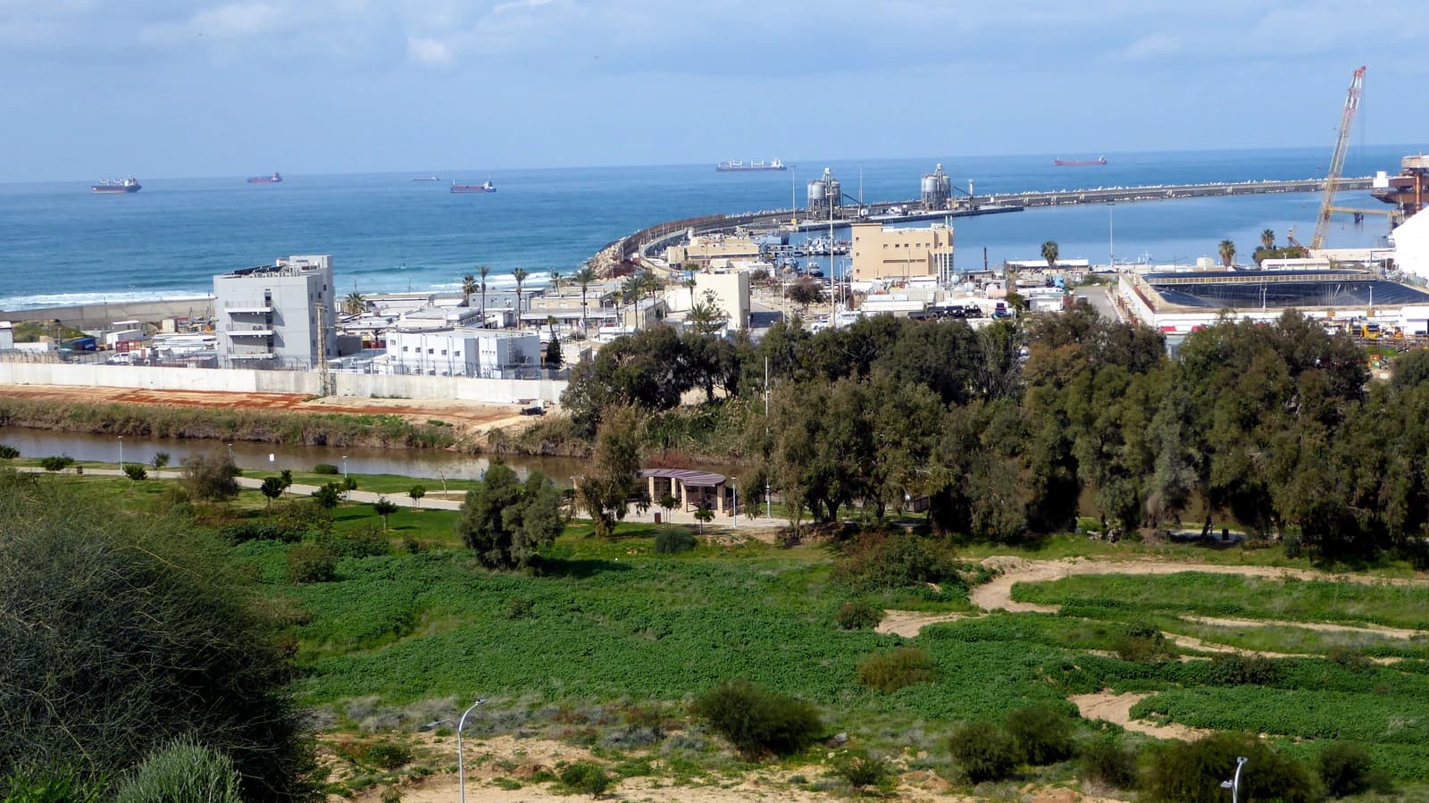 Ashdod Port with cargo ships on the horizon, a pier, and industrial buildings along the coast.