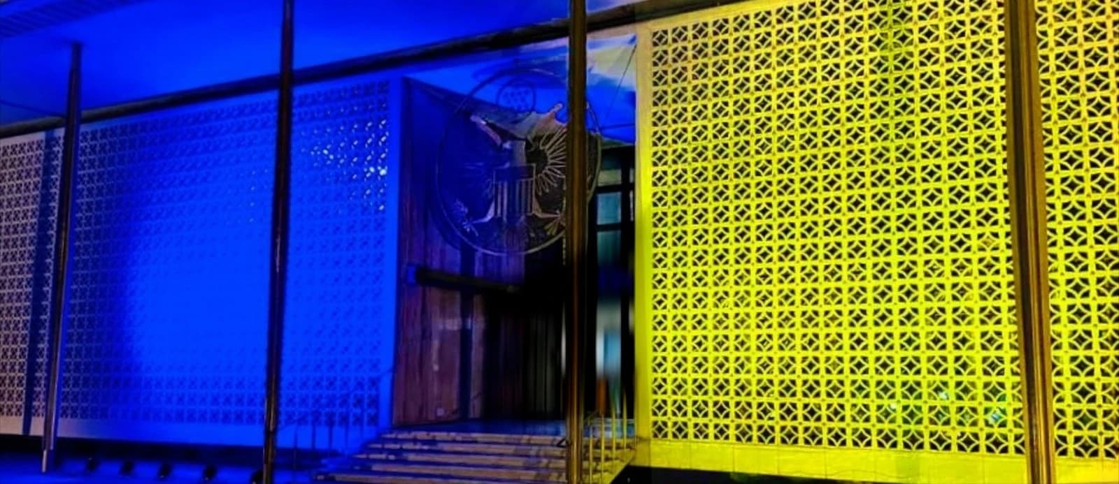 Exterior of the US Embassy in New Delhi illuminated with blue and yellow lights.
