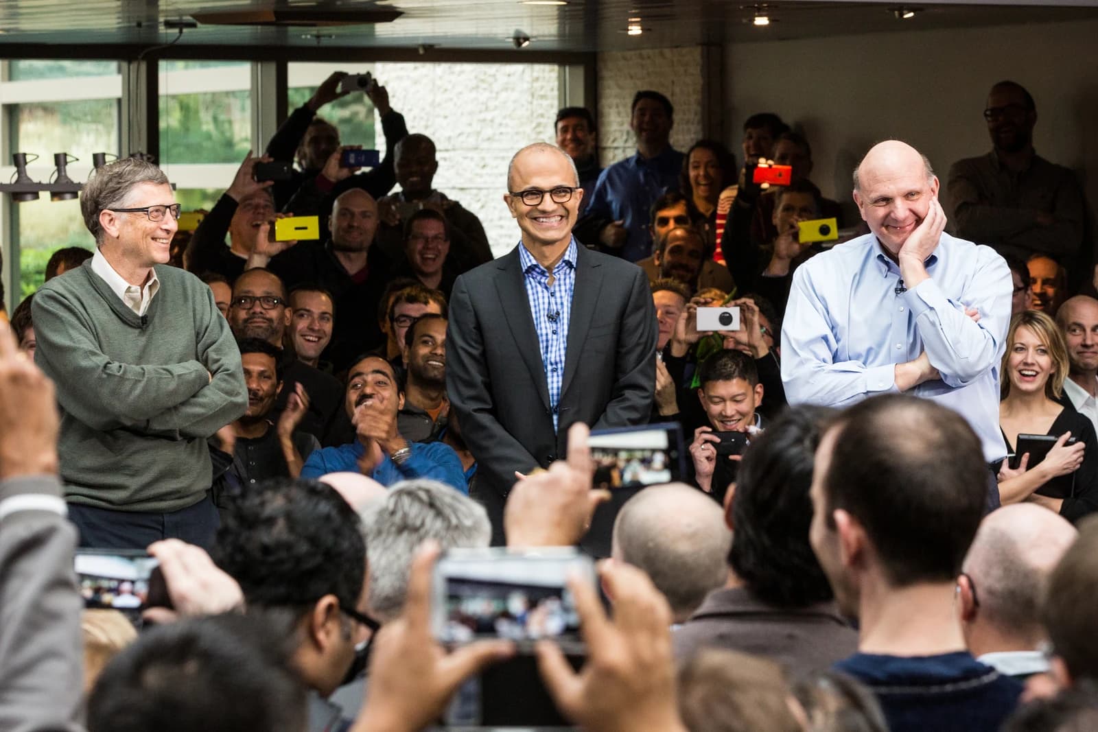 Satya Nadella, CEO of Microsoft, smiles with Bill Gates and Steve Ballmer among a crowd.