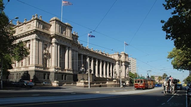 Parliament House in Melbourne, Victoria, with a red tram and horse-drawn carriage.