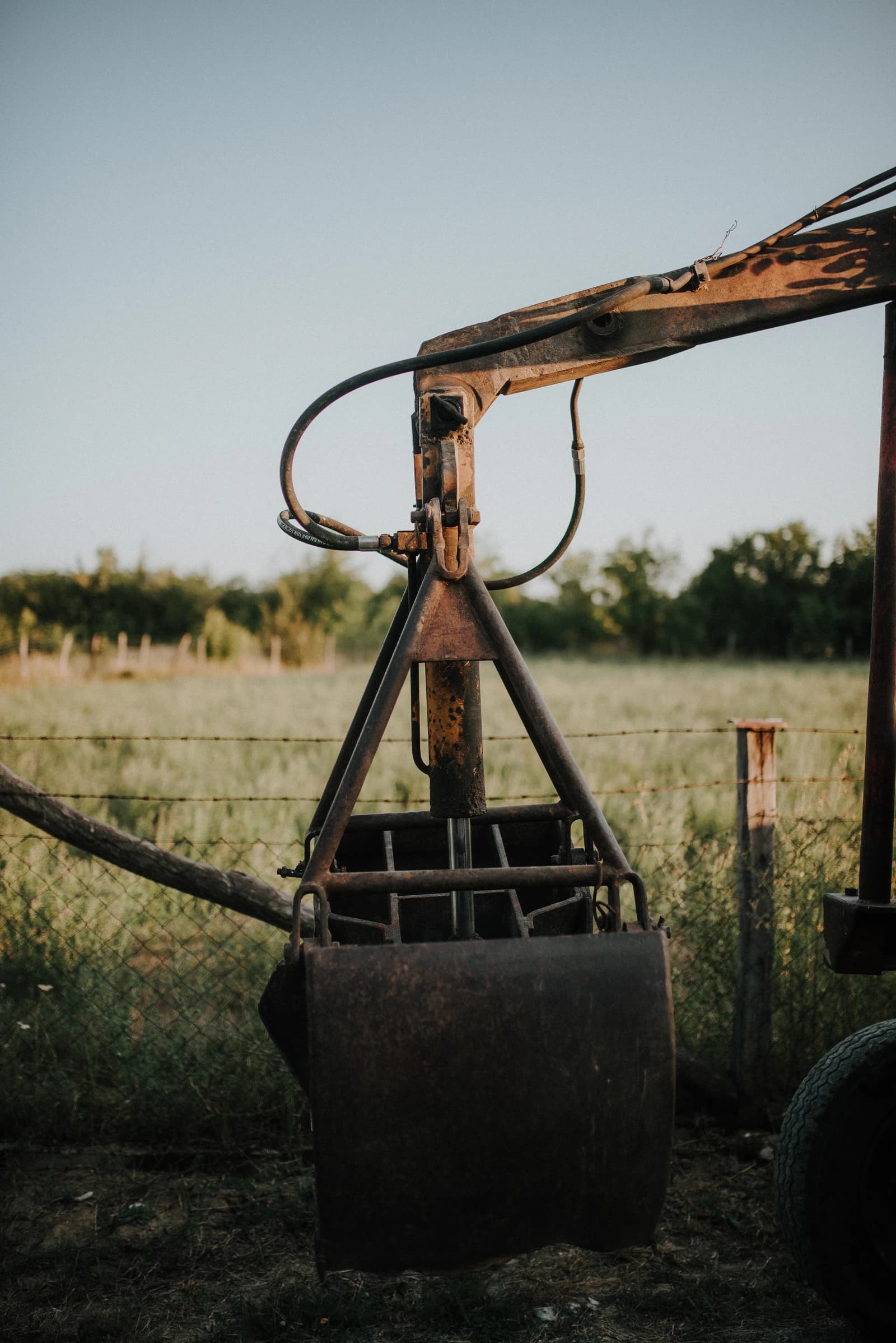 Rusty farming equipment, possibly a tractor scoop, standing in a field.