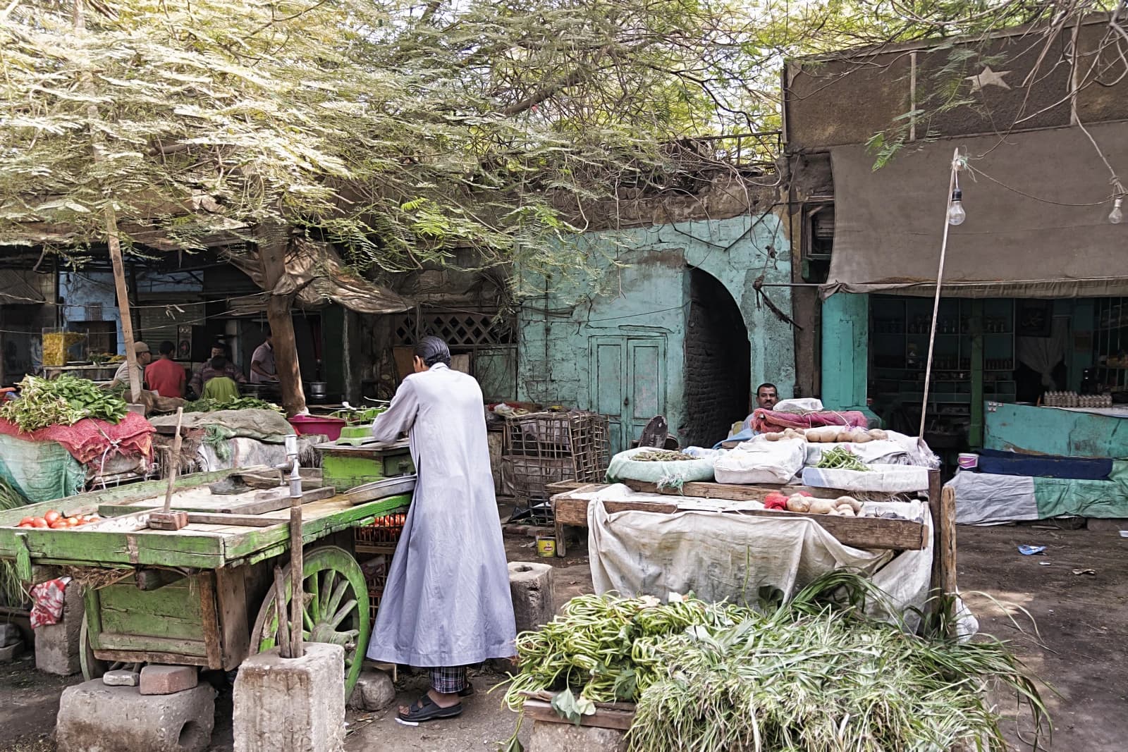 Man in long garment selling vegetables from a cart at an outdoor market.