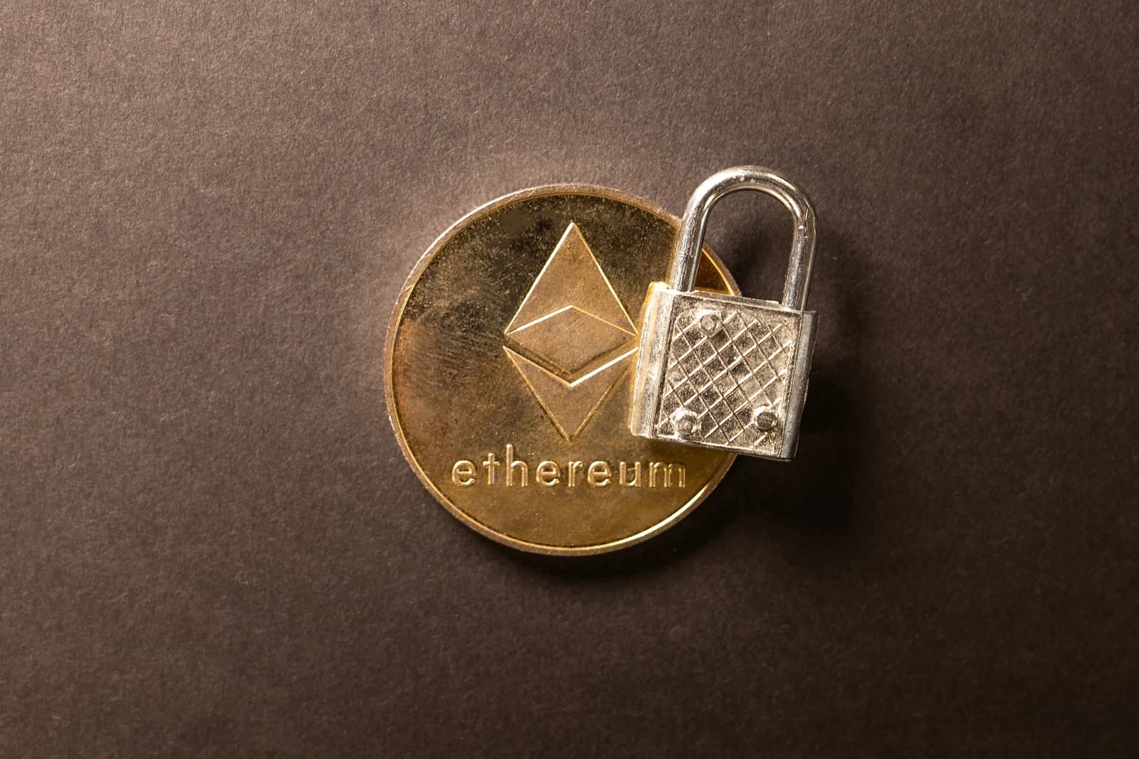 Close-up of a gold Ethereum coin with a small silver padlock on top.