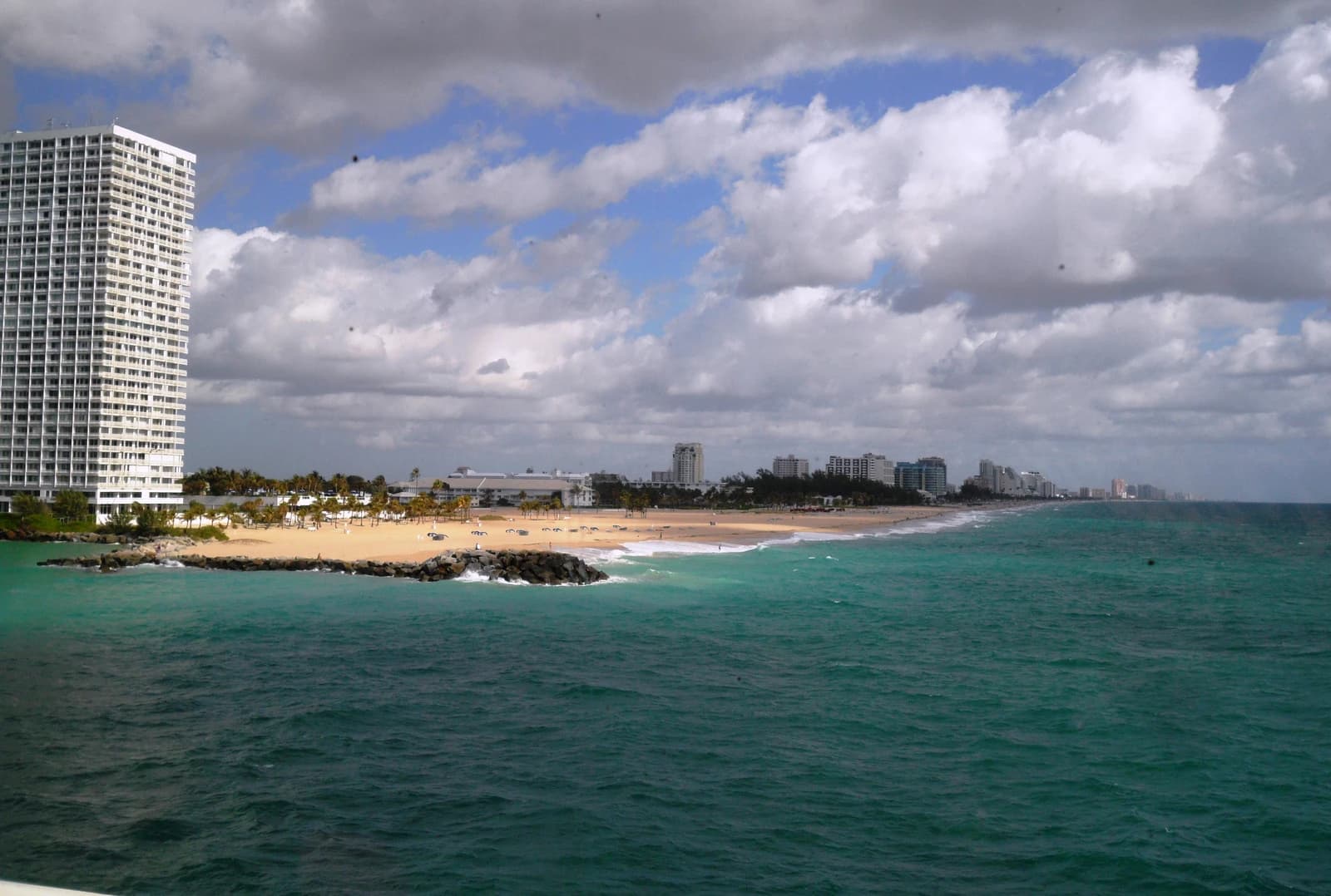 Beach and ocean with a tall white building on the left and a city skyline in the distance.