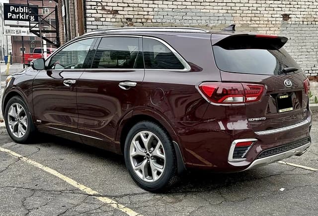 Burgundy Kia Sorento SUV parked on a paved street beside a brick building.