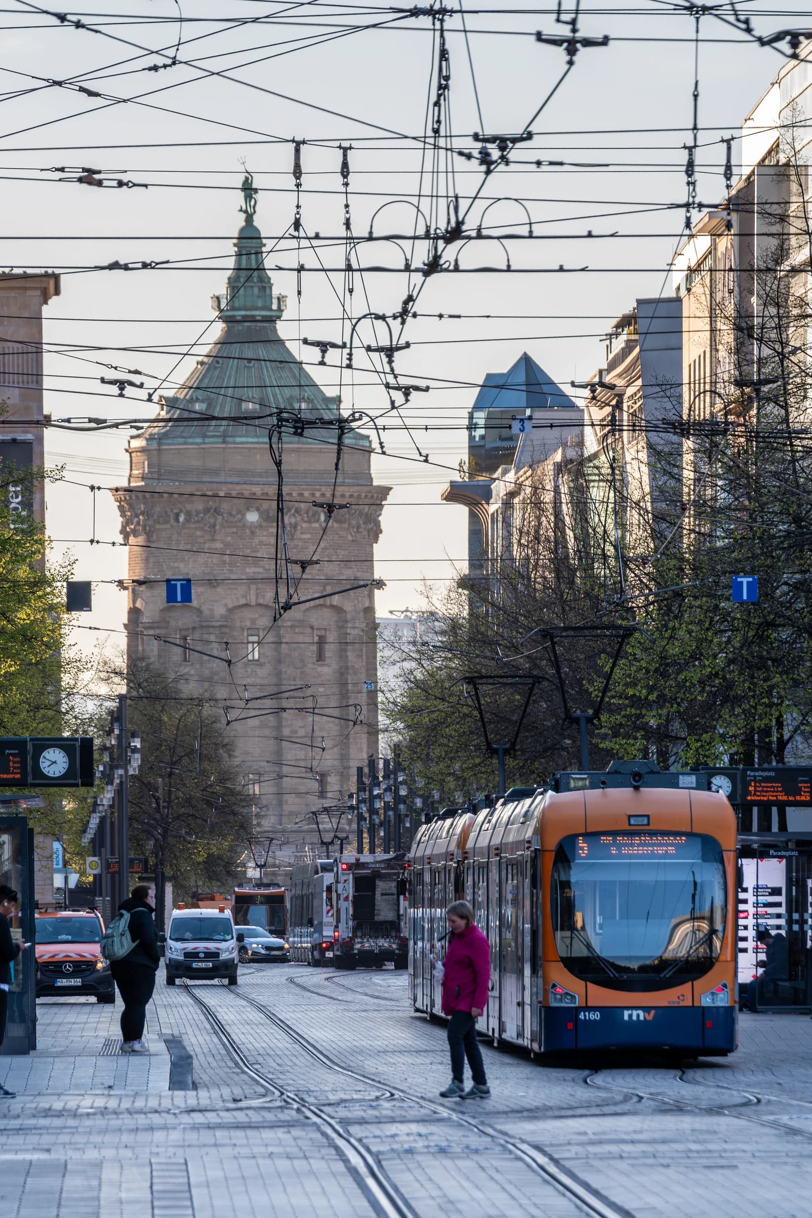 An orange tram travels down a street with a historic stone tower in the background.