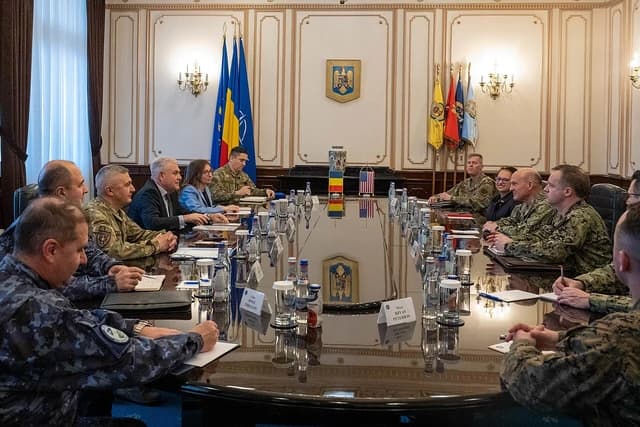 Military and civilian officials from Romania and the US at a large conference table.